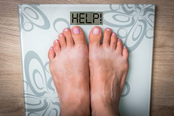 Woman's feet on a scale with word HELP! Food addiction