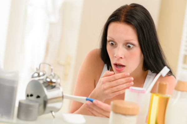 Shocked woman holding positive pregnancy test in the bathroom