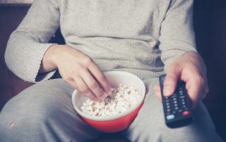 Person on couch eating popcorn and holding a remote