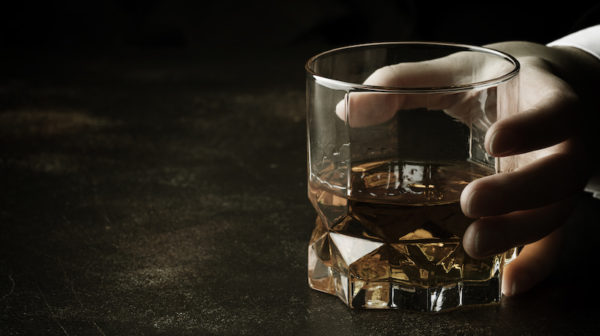 Glass of whiskey in person's hand/Adobe stock