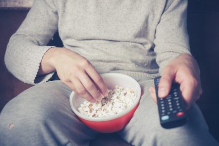 Person on couch eating popcorn and holding remote, no exercise